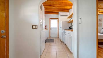 A narrow hallway leading to a kitchen with white cabinets, a wooden ceiling, and a door at the end.