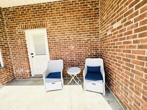A small patio area with two wicker chairs and a small round table, a white door, and a brick wall.