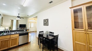 Een keuken met houten kastjes, een eettafel met stoelen, een inbouwoven en een plafondventilator.