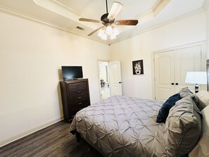 A bedroom with a bed, a dresser, a ceiling fan, a TV, and a door. - Villa 3, spacious townhouse in Tickfaw, LA (Tickfaw)