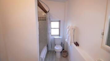 Un baño con inodoro, ventana, ducha y toallero.