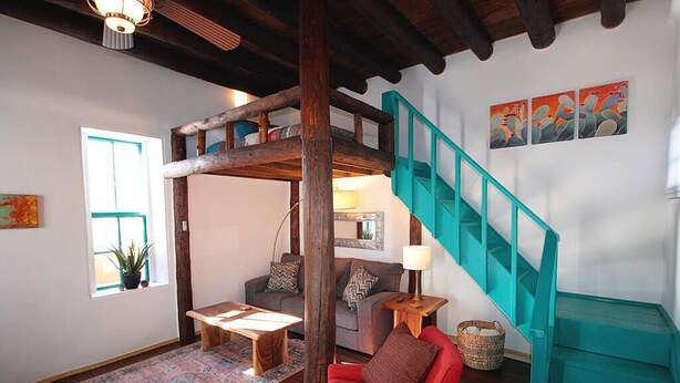 A cozy living room with a red sofa, wooden coffee table, and a teal staircase.