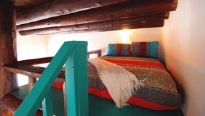 A cozy room with a wooden ceiling, a bed with colorful bedding, and a teal-colored chair.