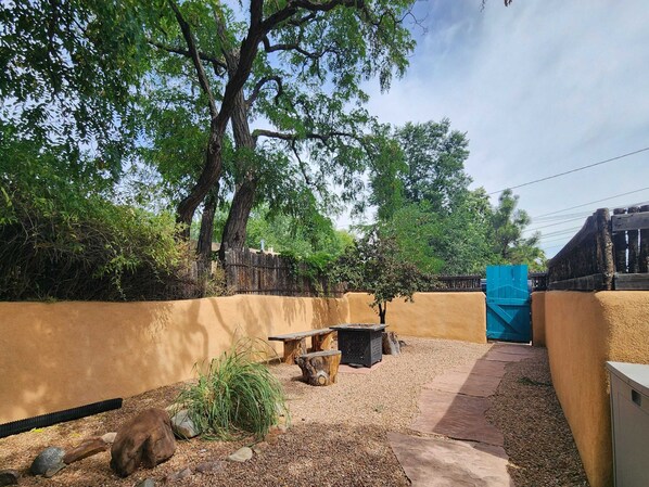 Un jardín con un banco de madera, una mesa pequeña y un árbol.