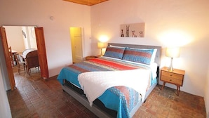 Quarto com cama, duas luminárias de cabeceira, ventoinha no teto e piso de madeira.