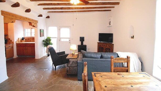 Uma sala de estar com piso de pedra, vigas de madeira no teto, televisão, sofá, mesa e lareira.