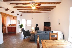 Una sala de estar con piso de piedra, vigas de madera en el techo, televisión, sofá, mesa y chimenea.