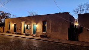Um edifício com várias portas e janelas, algumas iluminadas, e uma rua na frente.