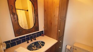 Un baño con tocador de madera, un lavamanos con azulejos decorativos, un espejo con marco ornamentado y un inodoro.