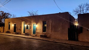 Un edificio con varias puertas y ventanas, algunas iluminadas, y una calle frente a él.