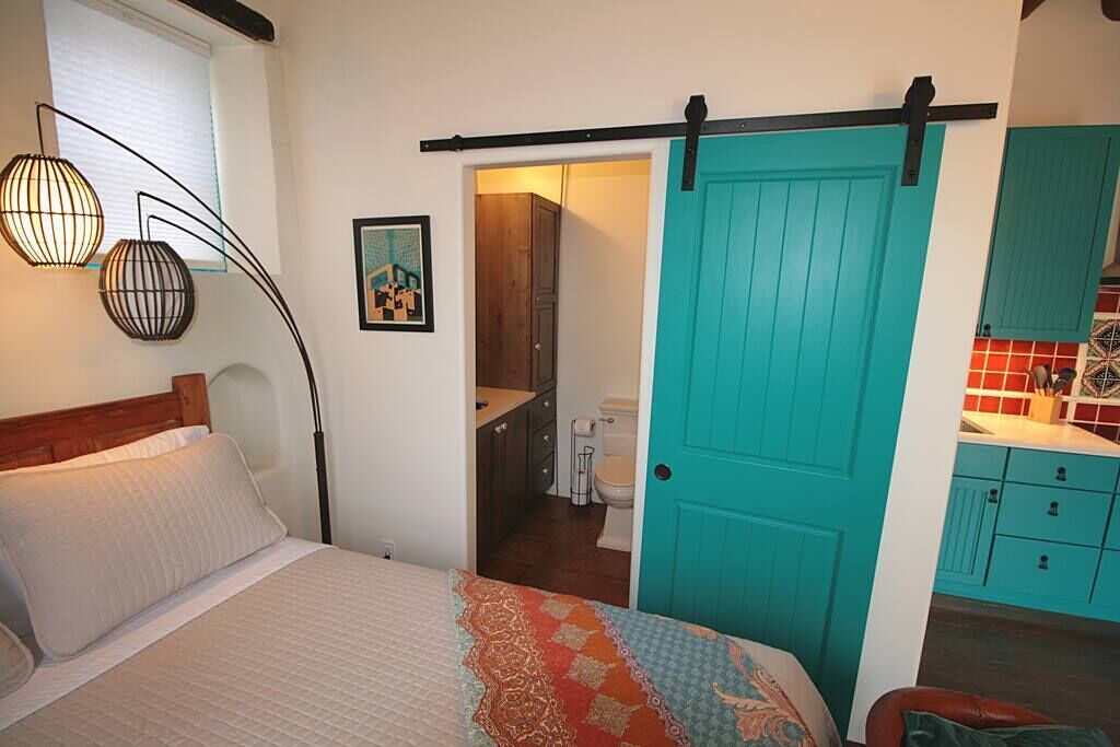 A bedroom with a bed, a door leading to a bathroom, and a kitchenette area.