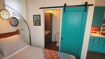 A bedroom with a bed, a door leading to a bathroom, and a kitchenette area.