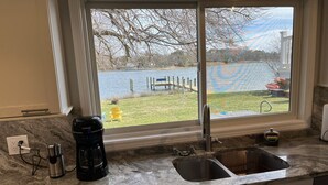 A kitchen with a large window, a sink, a coffee maker, and a small cabinet.