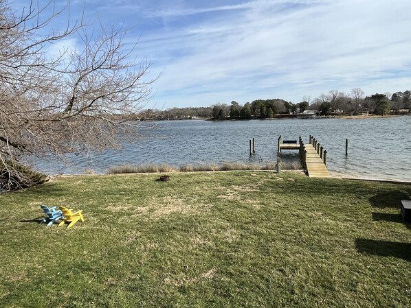 Un área con césped, un muelle que se adentra en un lago, árboles y un cielo despejado.