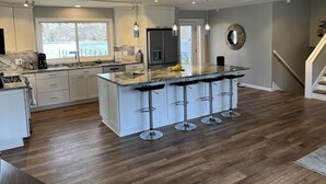 A modern kitchen with a central island, bar stools, and a large window overlooking a body of water.