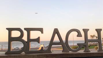 A sign with the word "BEACH" in large letters, overlooking a coastal area with a clear sky and a plane in the distance.