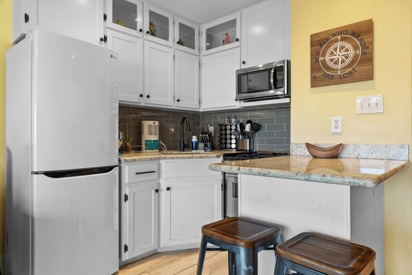 A modern kitchen with white cabinets, a microwave, and a stove. There are two stools and a wooden wall decor.