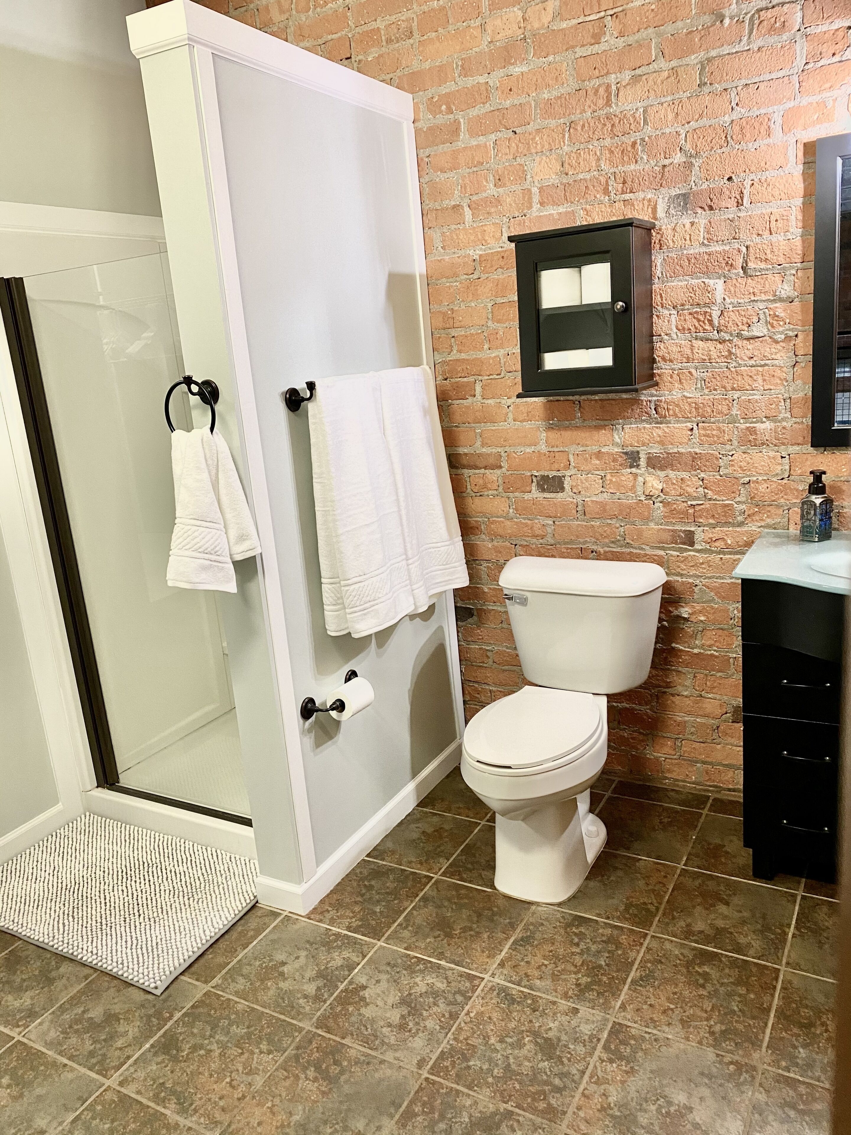 A bathroom with a glass shower enclosure, white toilet, and a black cabinet.