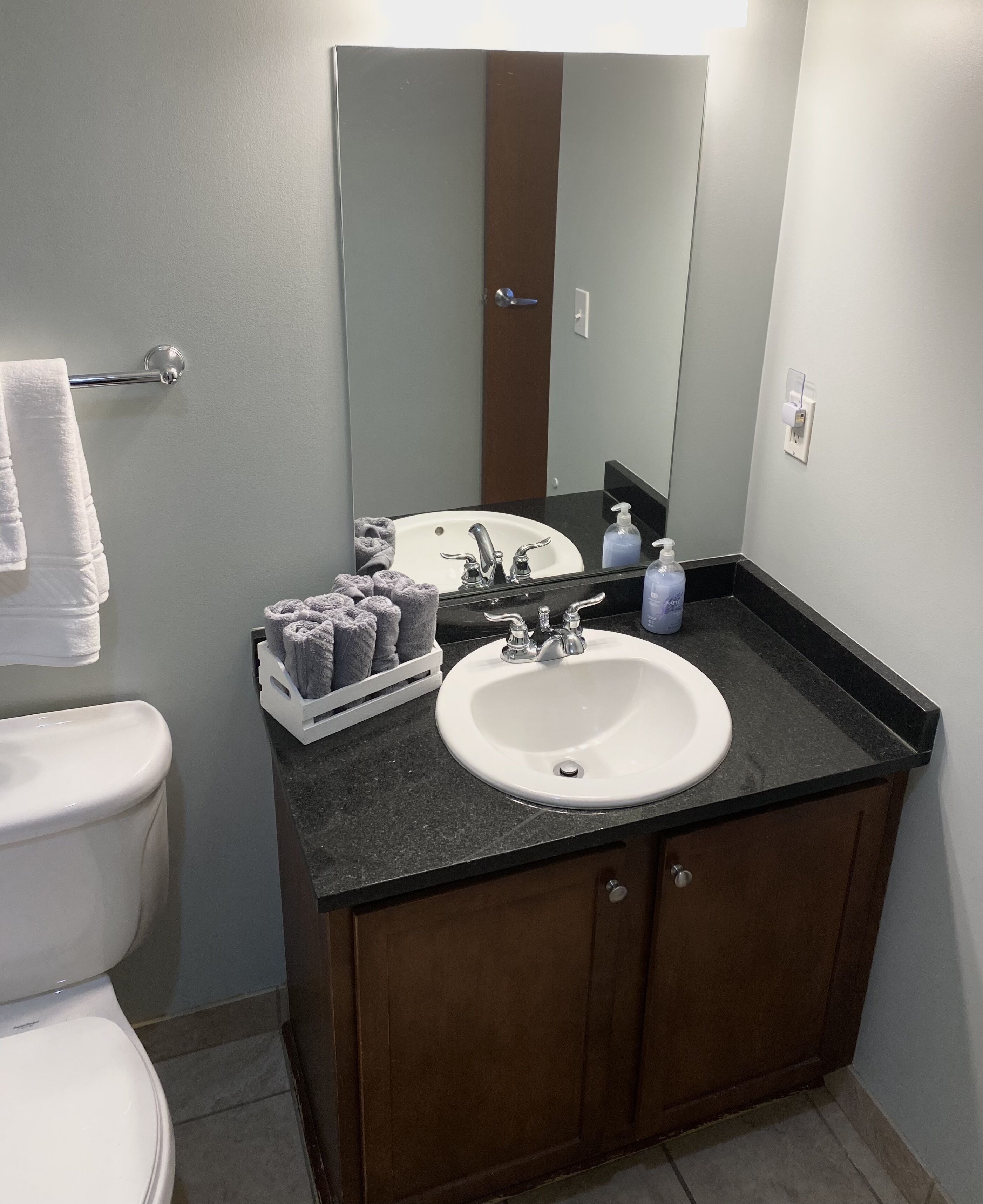 A bathroom with a white sink, dark countertop, wooden cabinet, and a mirror above the sink.
