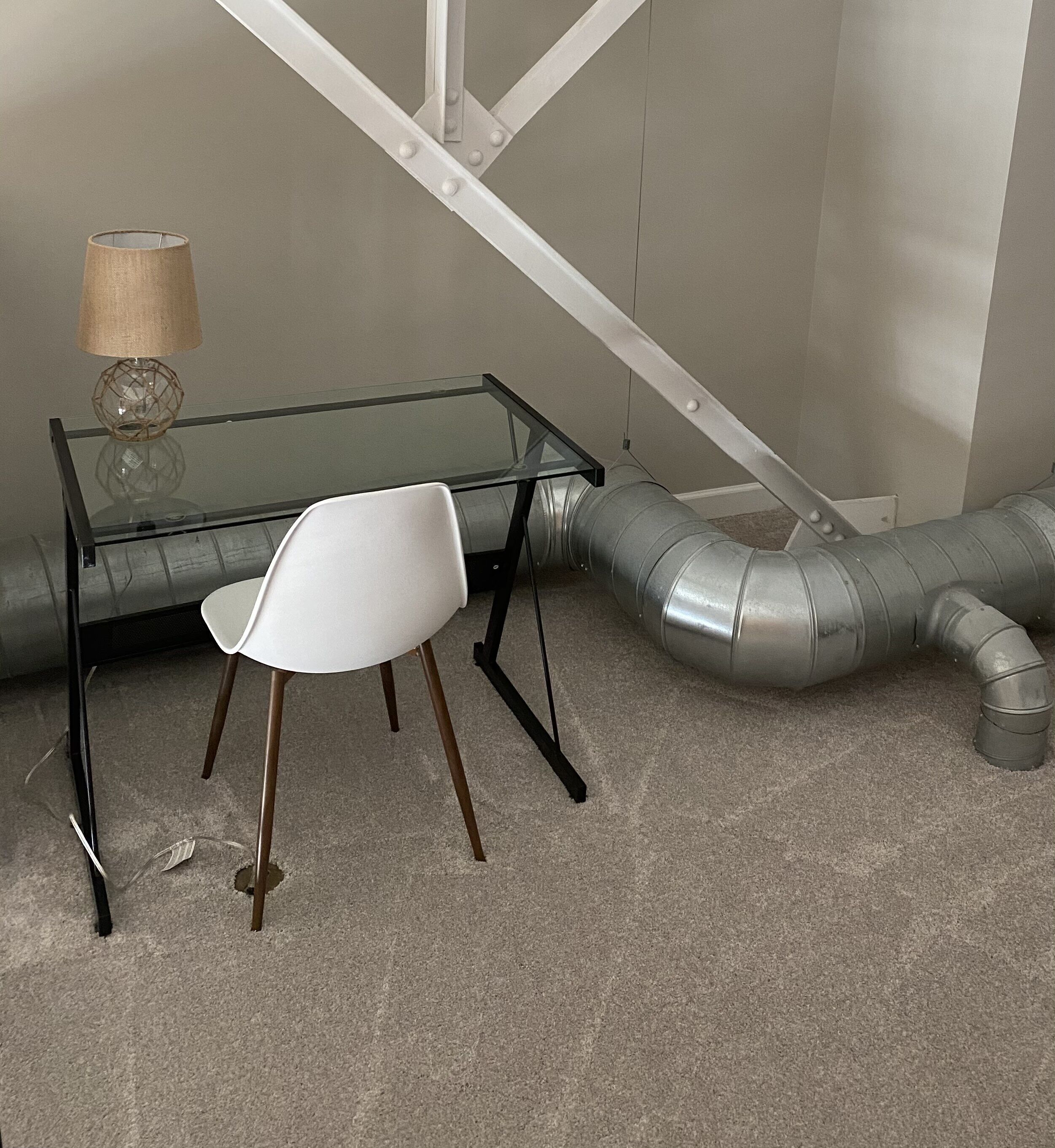 A modern room with a glass table and white chair, a lamp, and a visible ductwork system.