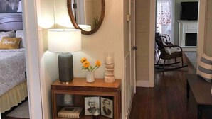 Une pièce chaleureuse avec un plancher en bois, une table de chevet avec une lampe, un miroir et une petite étagère ornée d’objets décoratifs.