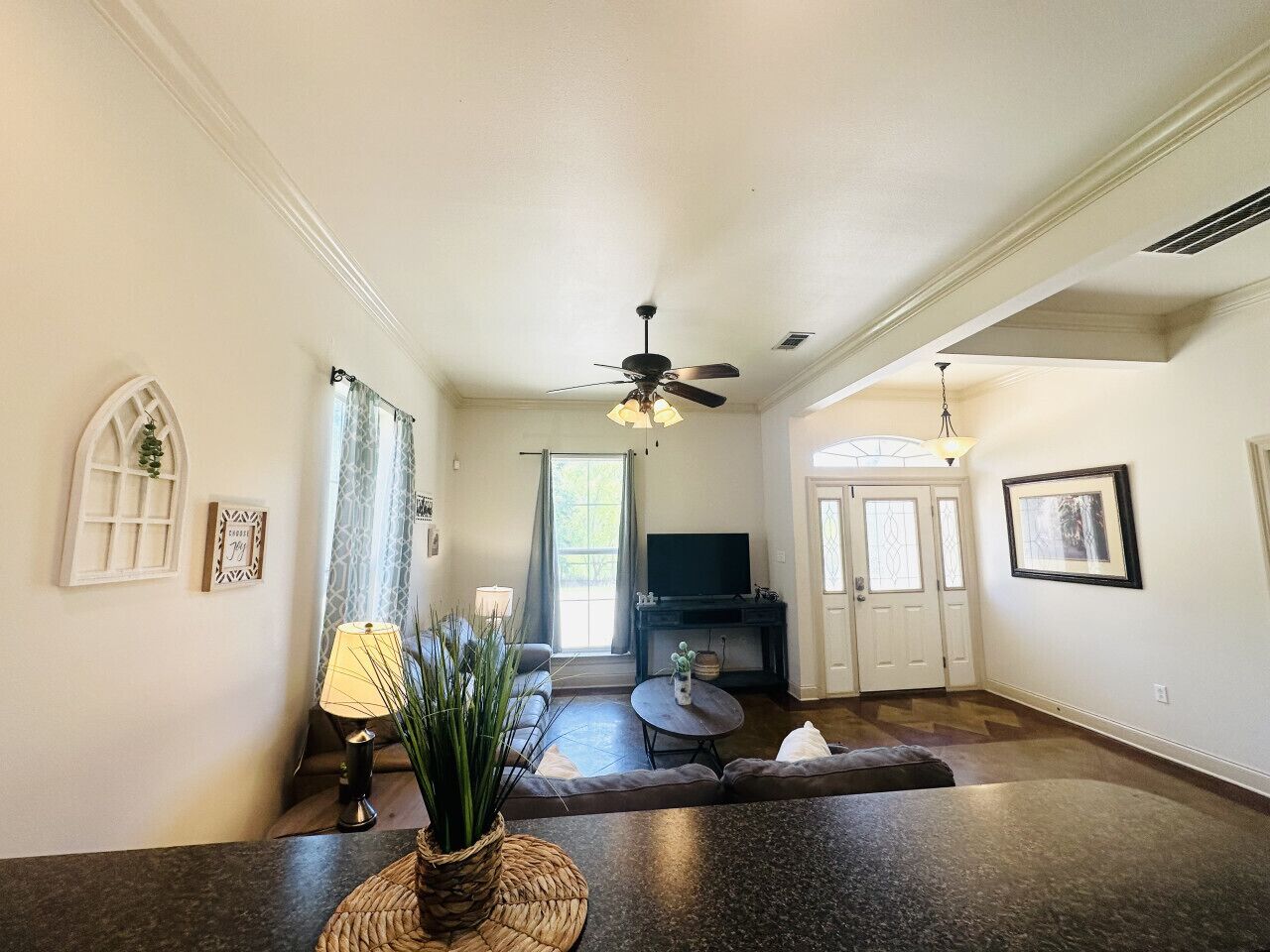 A spacious living room with a dark floor, a ceiling fan, a TV, and a dining area with a table and chairs.