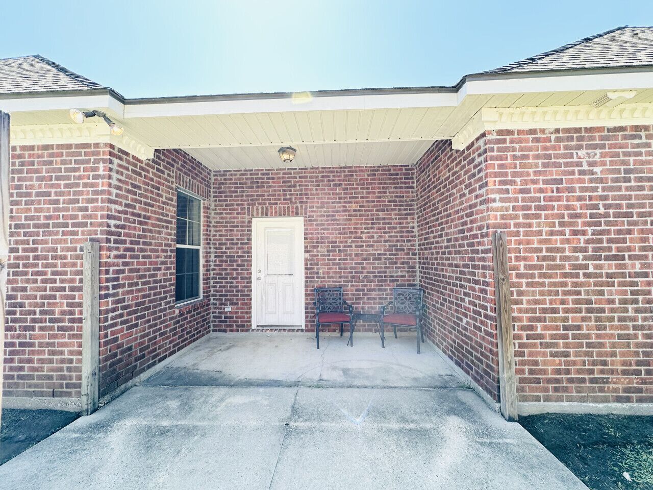 A brick building with a covered patio area, a door, and two chairs.