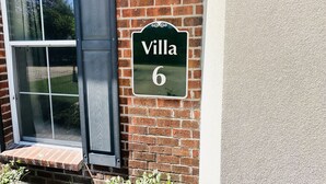 En tegelvägg med en grön skylt där det står ”Villa 6”.