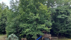 A backyard with a wooden deck, a slide, and a seating area with Adirondack chairs. - Warm Secluded Adirondack Chalet with Game Room and Bar/Lounge (Warrensburg)