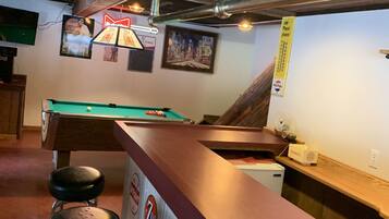 A bar area with a pool table, stools, and various posters.
