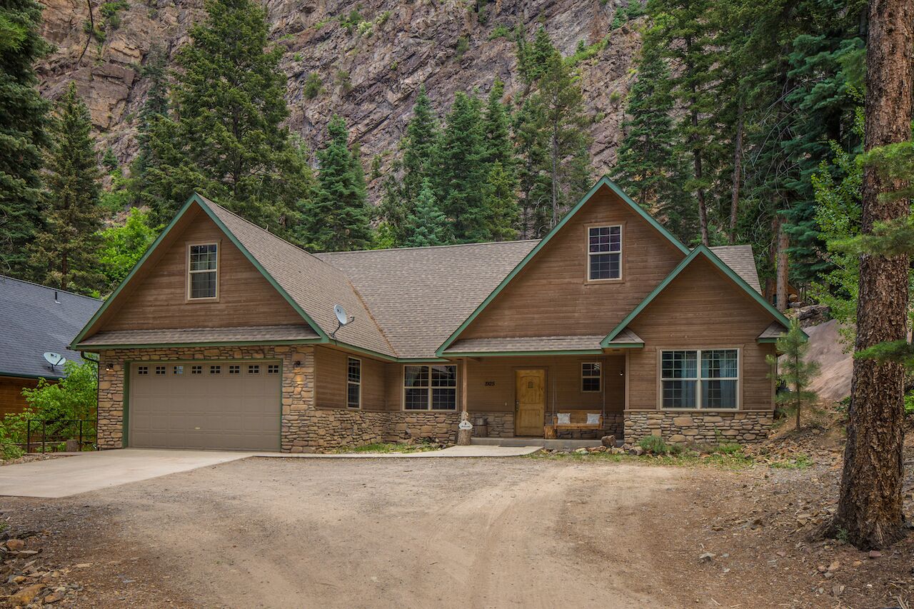 A two-story log cabin with a stone foundation, a garage, and a front porch.