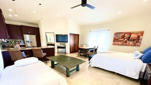A hotel room with two beds, a dining table, and a kitchen area.