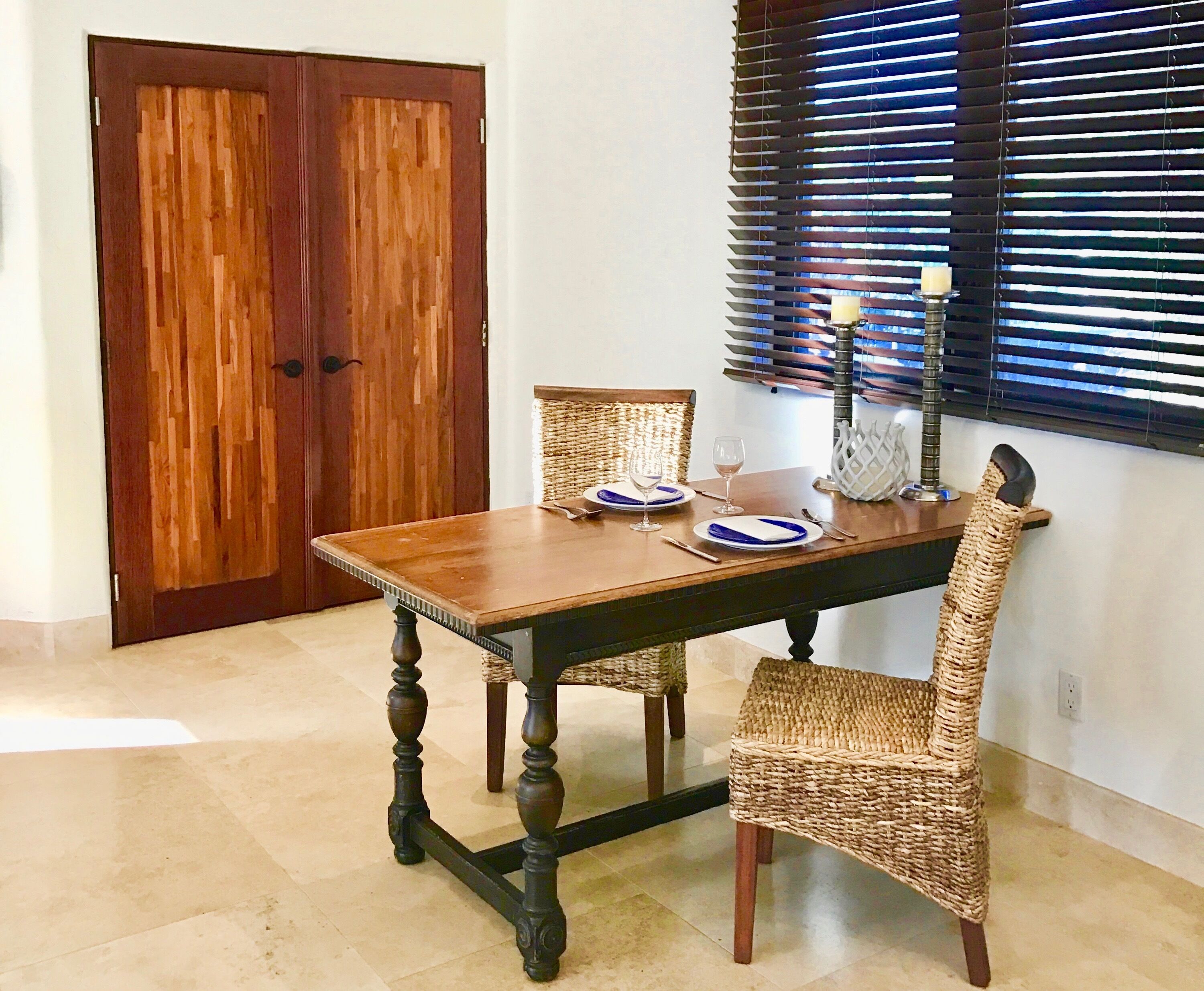Uma mesa de jantar com cadeira de fibra, taça de vinho e castiçal.