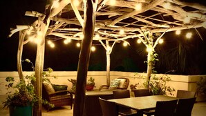 An outdoor patio with a pergola, string lights, wicker furniture, and potted plants.