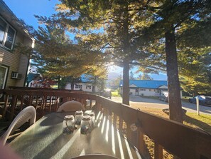 Une terrasse en bois avec une table et des chaises, entourée d’arbres et sous un ciel dégagé.