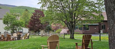 A patio area with wooden chairs and a table, surrounded by trees and a grassy lawn.