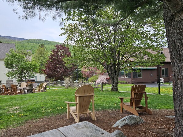 A patio area with wooden chairs and a table, surrounded by trees and a grassy lawn.