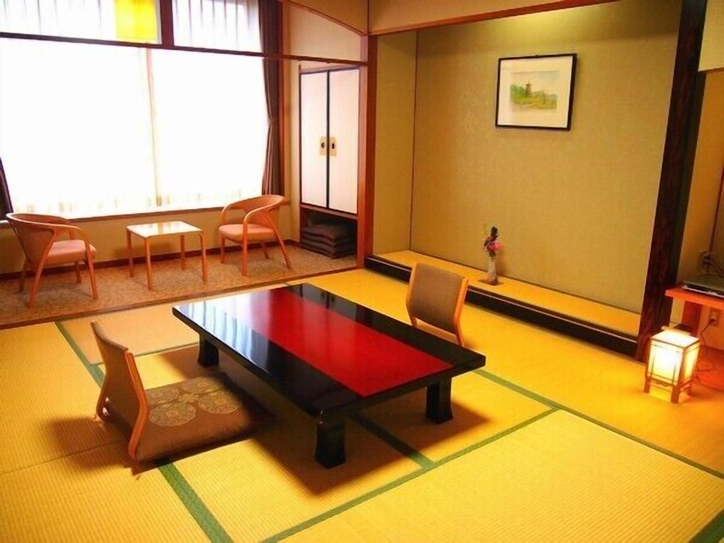 A tatami mat room with a low table, chairs, and a small table with a lamp.