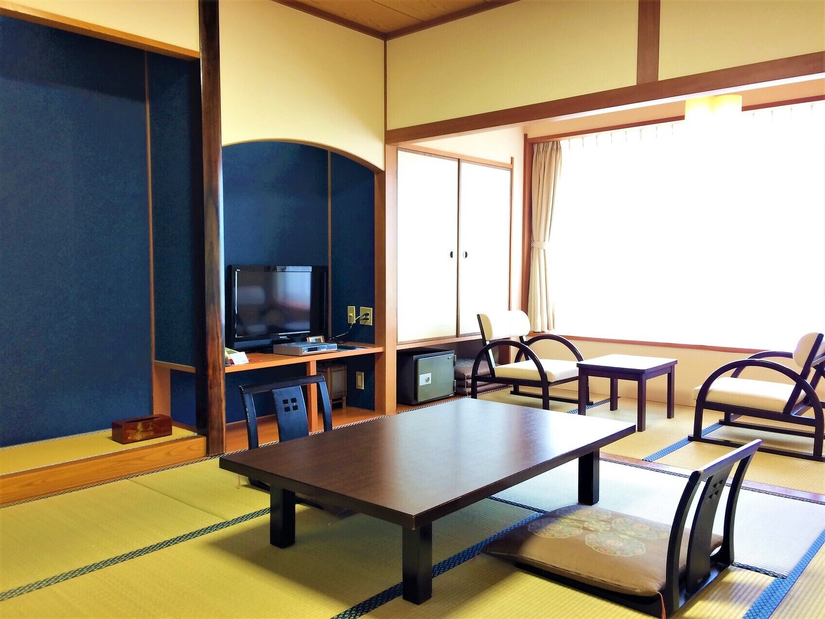 A traditional tatami mat room with a television, seating, and a view of the outside.