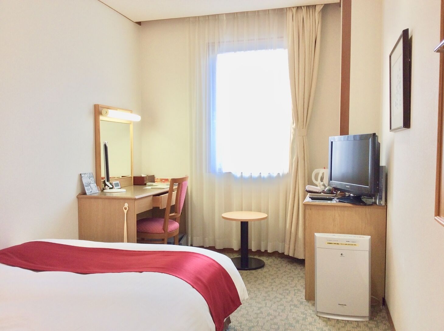 A hotel room with a bed, a desk with a chair, a television, and a small table.