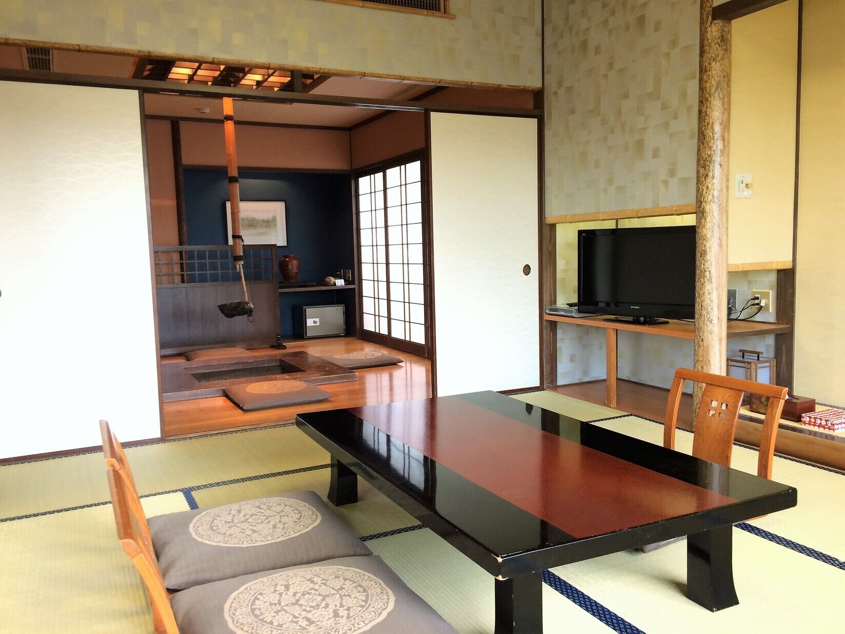 A traditional Japanese room with tatami flooring, a low table, and a television on a wooden stand.