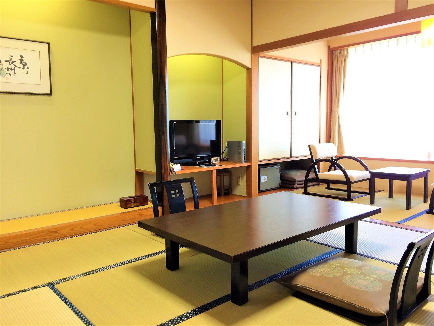 A traditional Japanese-style room with tatami flooring, a low table, a television, and a chair.