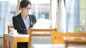 Iemand zit aan een tafel met een laptop, een kopje en een menukaart.