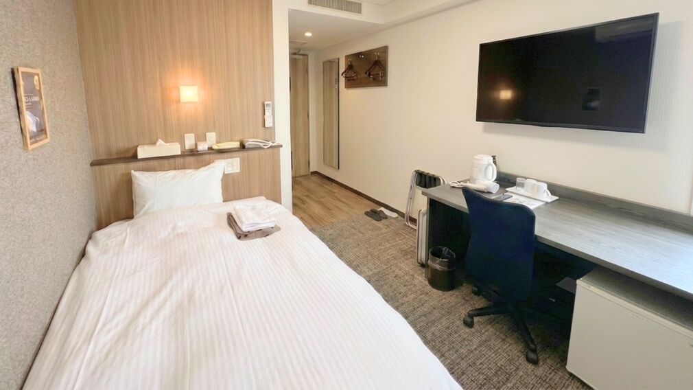 A hotel room with a bed, a desk, a chair, a television, and a coffee maker.