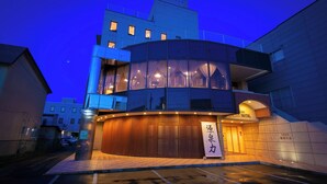 Een modern hotel met een gebogen gevel, grote ramen en een bord in Japanse tekst.