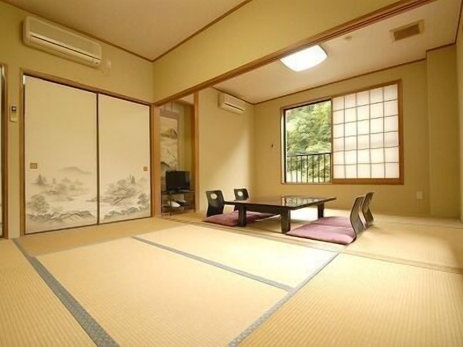 A tatami mat room with a sliding door, a small table, chairs, and a window with a view of greenery.