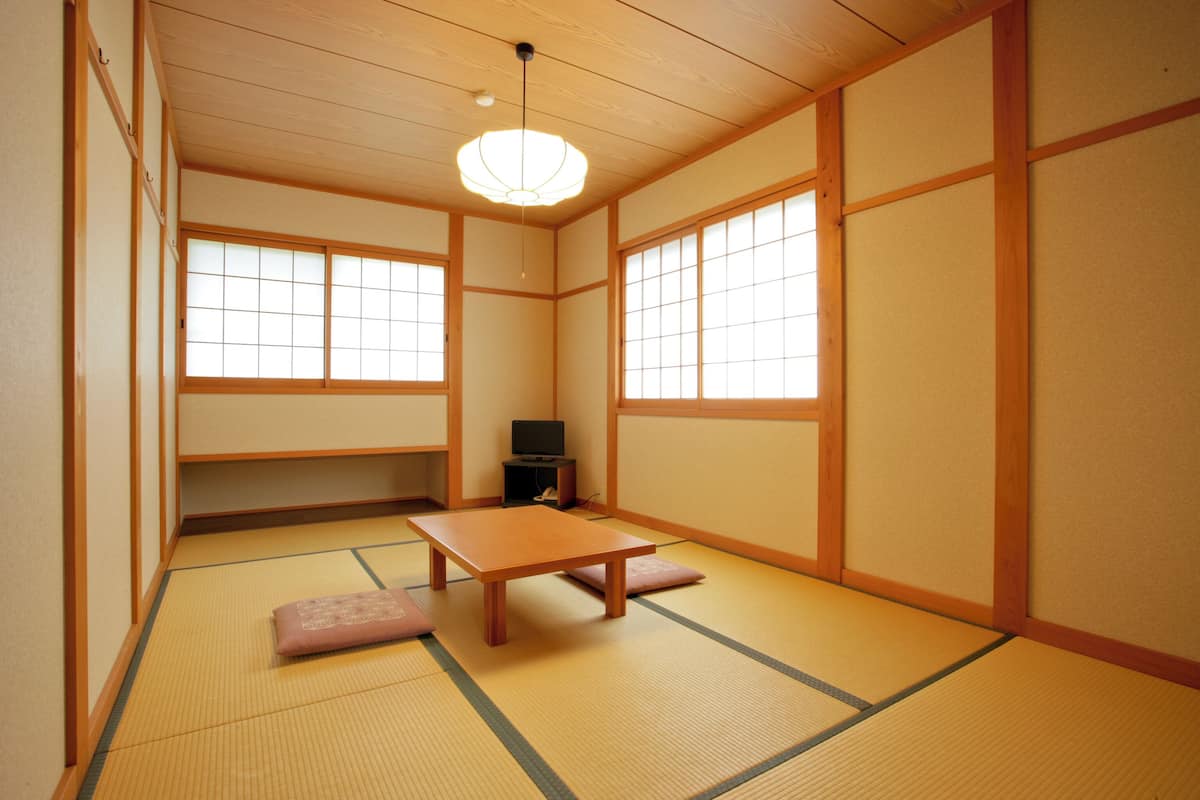 A traditional Japanese room with tatami flooring, a low table, cushions, sliding doors, and a ceiling light fixture.