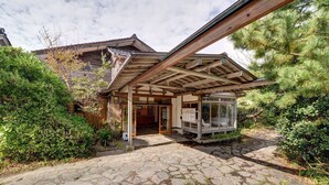 A traditional wooden building with a stone-paved entrance, surrounded by dense greenery. - Sakataya Ryokan (Yuza)