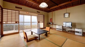 A traditional Japanese room with tatami flooring, a low table, a bench, a television, and a heater. - Sakataya Ryokan (Yuza)