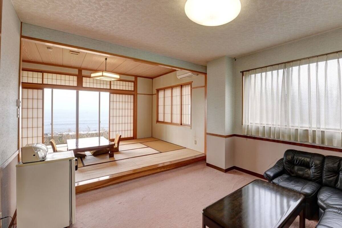 Una habitación japonesa tradicional con suelo de tatami, un sofá de cuero negro, una mesita y un refrigerador.